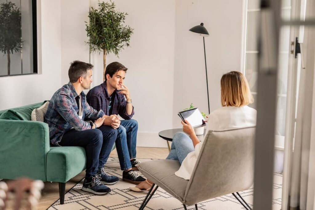 Two men sitting on a green couch speaking to a couples therapist